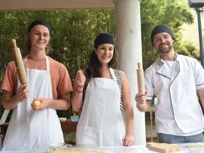 Three smiling Spanish students in a Toucan Spanish cooking class in Cali, wearing aprons and holding rolling pins, ready to learn Spanish as they cook.